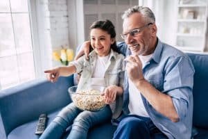 The little girl and a grandfather wathing television with a popcorn.